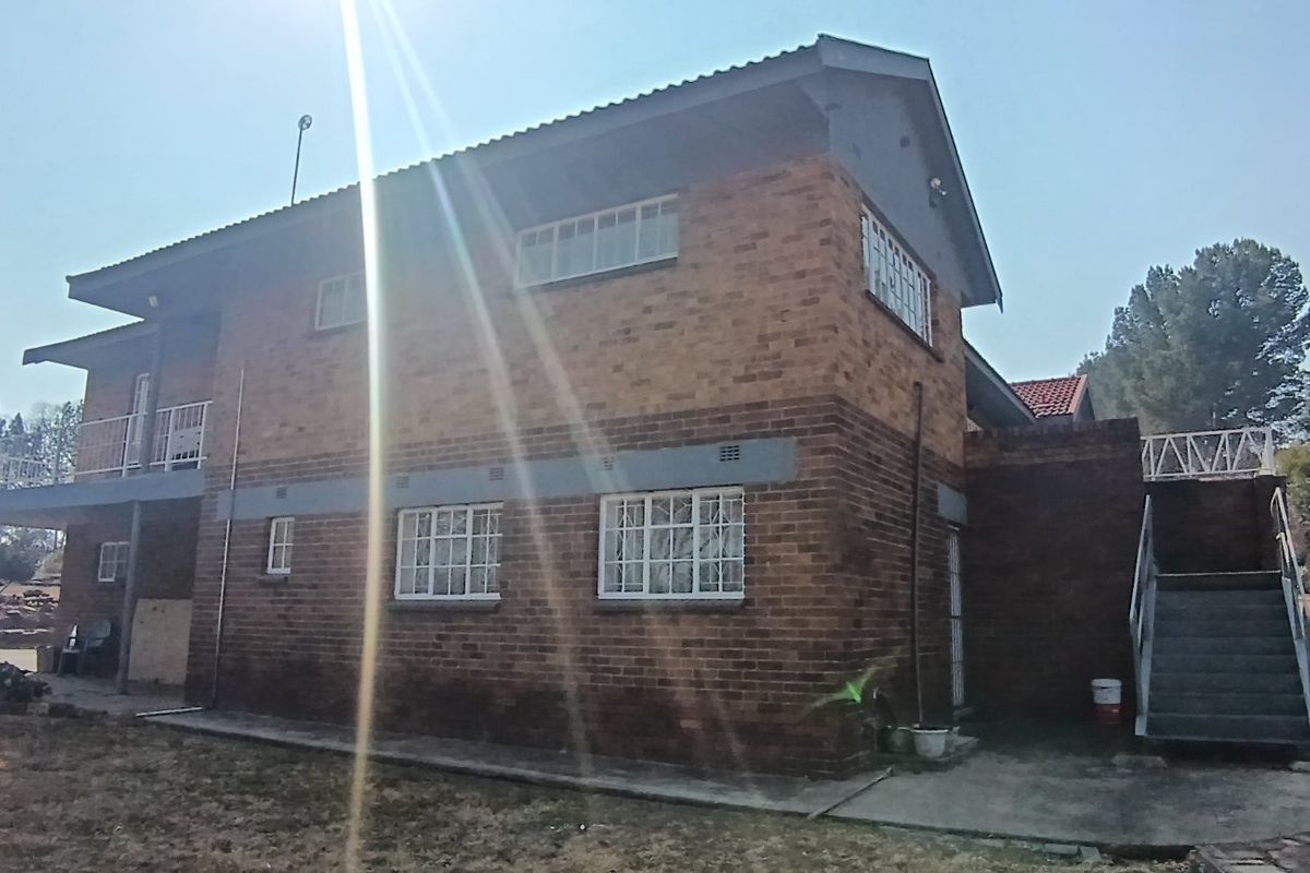 Rear view of a double-story brick house featuring an external staircase, balcony, and security bars on windows.