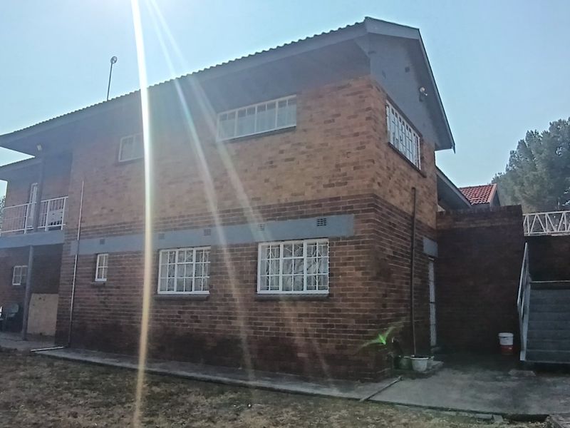 Rear view of a double-story brick house featuring an external staircase, balcony, and security bars on windows.