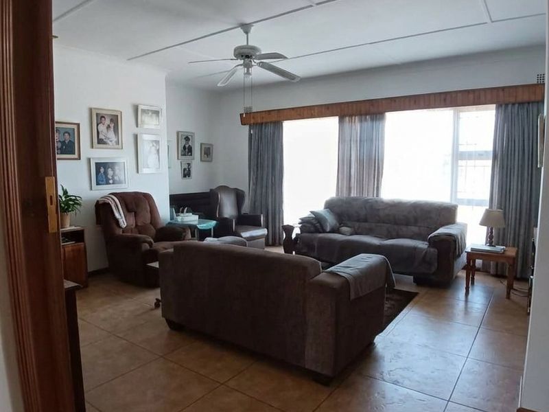 A spacious living room featuring tiled flooring, a ceiling fan, and large windows with timber pelmets, offering a comfortable and functional living space.