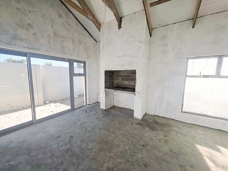 An unfinished living area featuring a vaulted ceiling with exposed beams, a built-in indoor braai, and large sliding glass doors leading to the exterior.