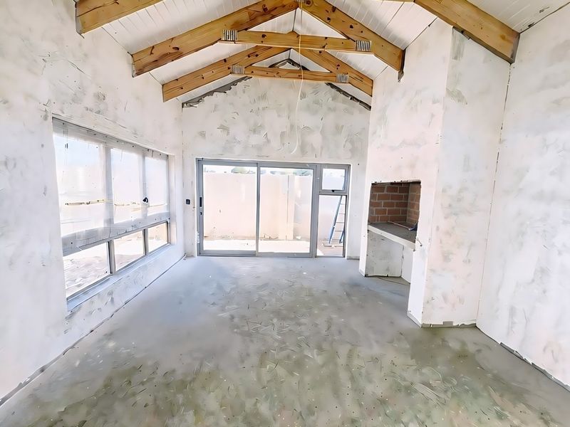 An unfinished living area featuring vaulted ceilings with exposed timber trusses, a built-in fireplace, and large sliding doors leading to the exterior.
