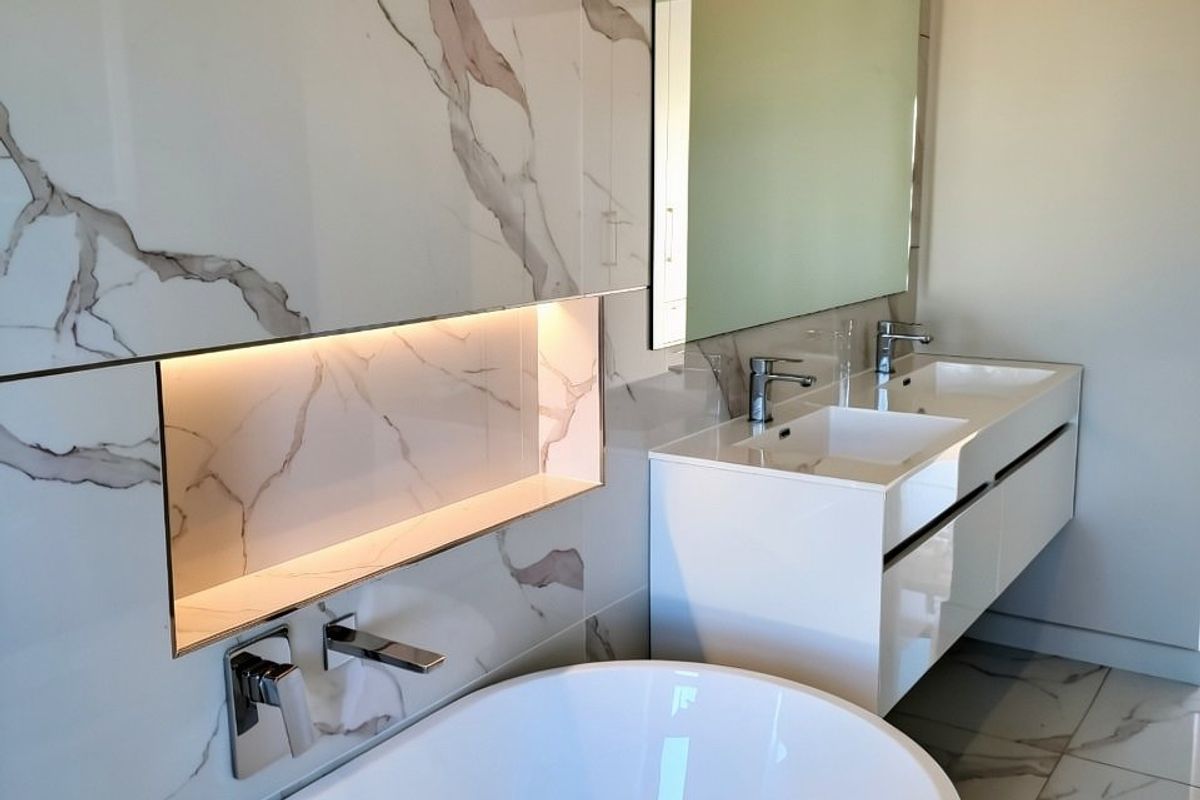 Modern luxury bathroom featuring a sleek freestanding bathtub, double vanity with wall-mounted faucets, and elegant marble-look tiling with integrated accent lighting.