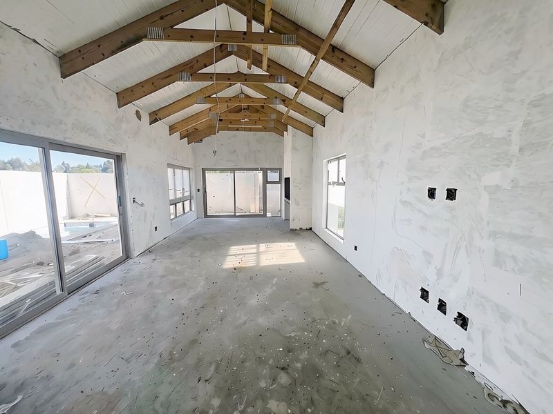 An unfinished open-plan living area featuring vaulted ceilings with exposed timber trusses, large sliding glass doors, and raw concrete flooring awaiting final finishes.