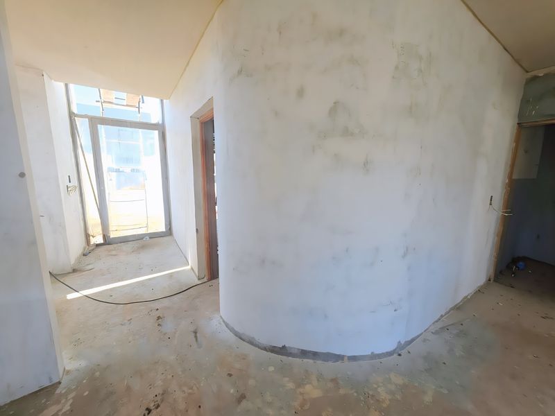 An unfinished interior hallway featuring a distinctive curved wall, concrete flooring, and an aluminium-framed glass door leading to an exterior space.