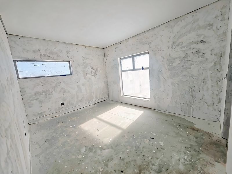 An unfinished bedroom space featuring bare plastered walls and concrete flooring, awaiting final finishes and flooring installation.