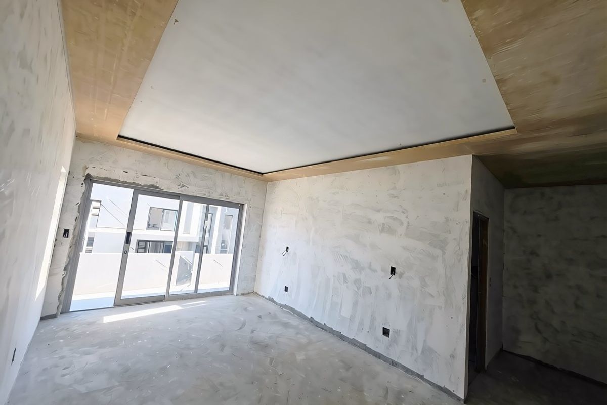An unfinished living room space featuring a recessed ceiling design and large sliding glass doors leading to an outdoor area.
