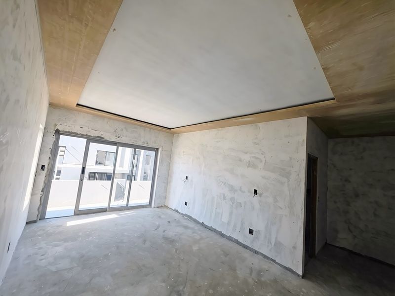 An unfinished living room space featuring a recessed ceiling design and large sliding glass doors leading to an outdoor area.