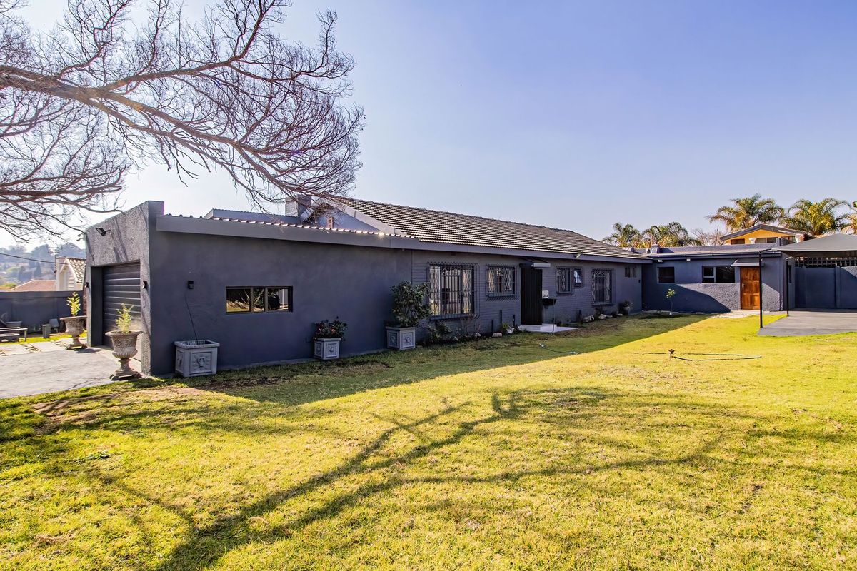 A well-maintained rear exterior view of the house featuring a spacious lawn, paved driveway, and secure garage access.