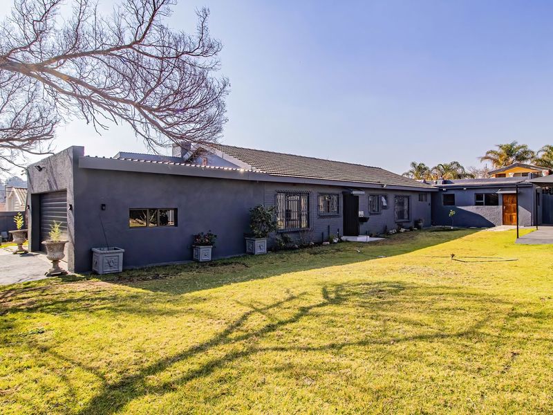 A well-maintained rear exterior view of the house featuring a spacious lawn, paved driveway, and secure garage access.