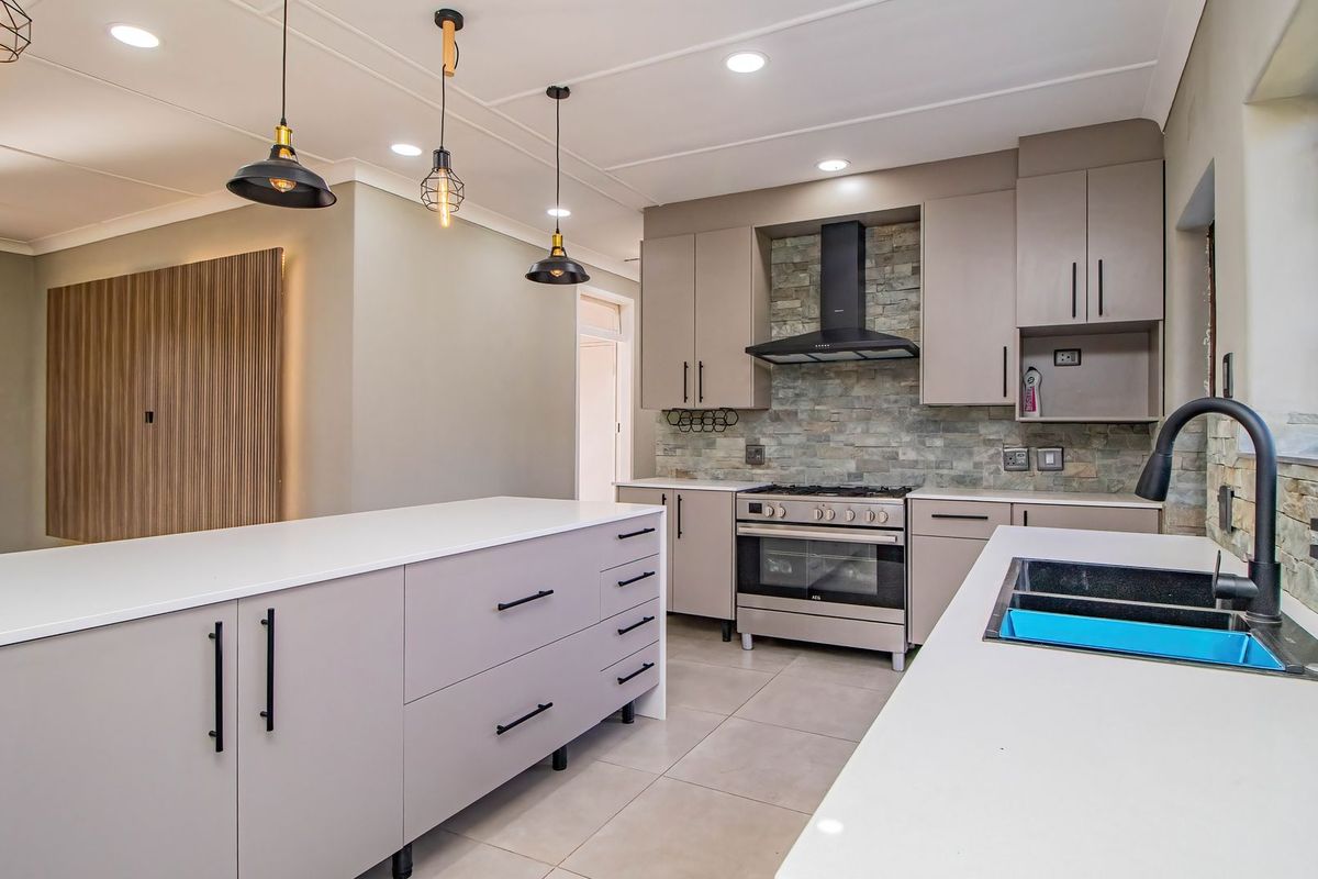 Modern kitchen featuring a large island, stone splashback, gas stove with extractor, and sleek built-in cabinetry with contemporary finishes.