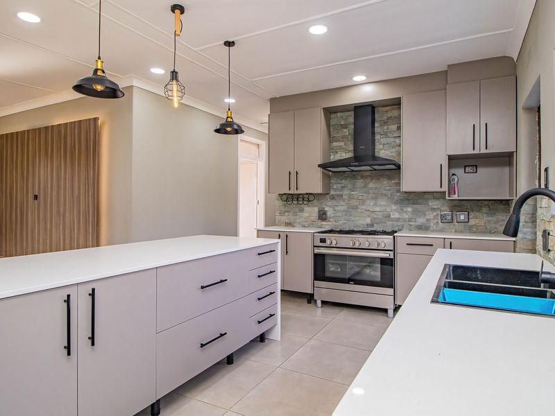 Modern kitchen featuring a large island, stone splashback, gas stove with extractor, and sleek built-in cabinetry with contemporary finishes.