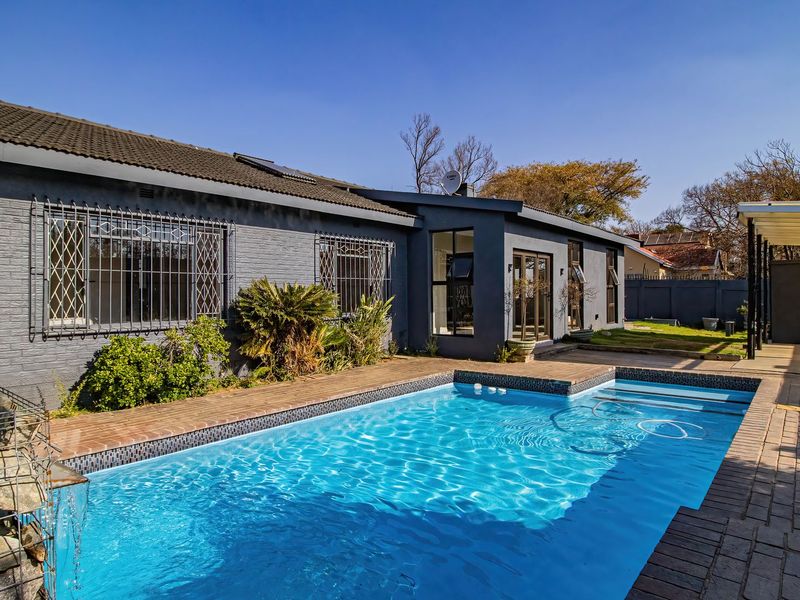 A well-maintained rear exterior featuring a swimming pool with a tiled surround and an adjacent covered patio area.