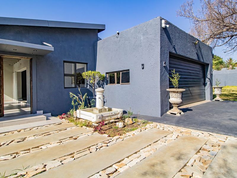 Modern front facade featuring a dark grey textured finish, integrated garage, stone-paved driveway, and a decorative water feature at the entrance.