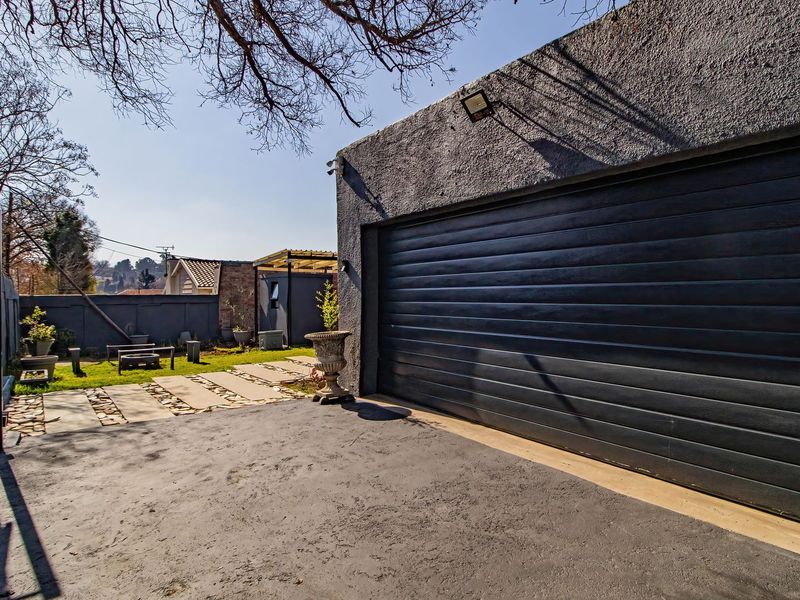 A view of a modern garage with a dark sectional door, paved driveway, and secure perimeter fencing in a well-maintained outdoor setting.