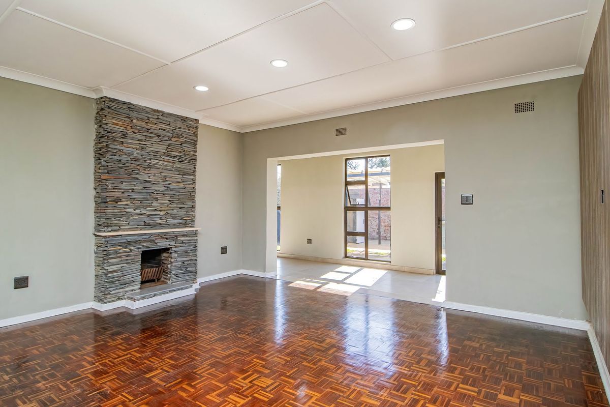 Spacious living room featuring classic parquet flooring, a striking stone fireplace, and recessed lighting, offering a bright and open atmosphere.
