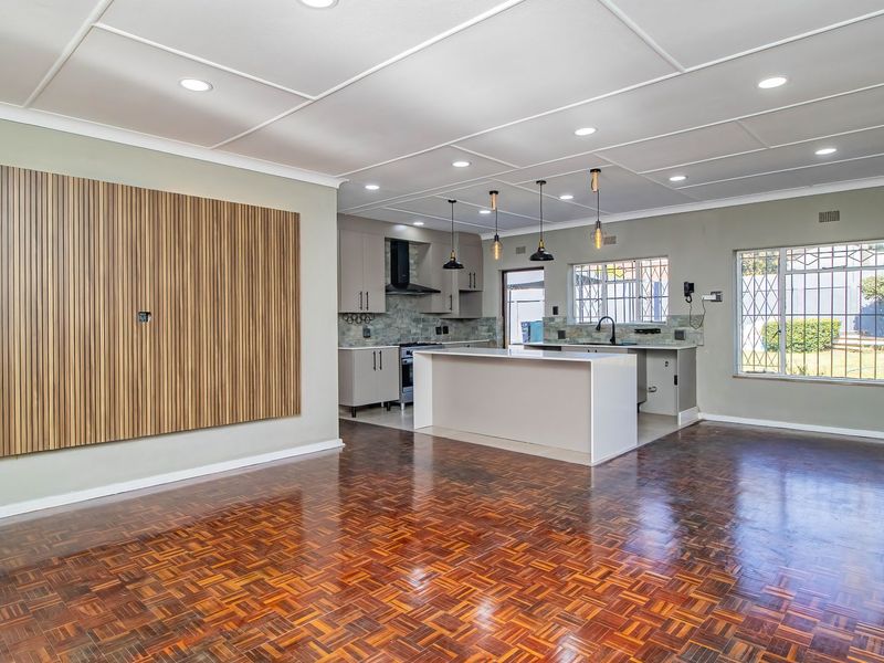 Spacious open-plan living and kitchen area featuring polished parquet flooring, a modern kitchen island, and stylish feature wall paneling.