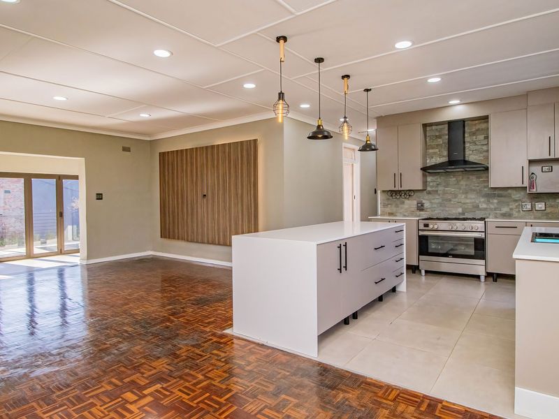 Spacious open-plan living and kitchen area featuring a modern kitchen island, gas stove, parquet flooring, and recessed lighting, leading to an outdoor patio.