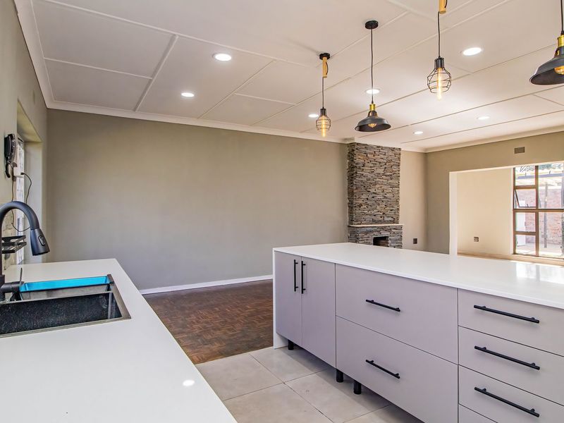 Modern open-plan kitchen featuring a large island with stone countertops, sleek cabinetry, and a striking stone feature wall, flowing into an adjacent living area.