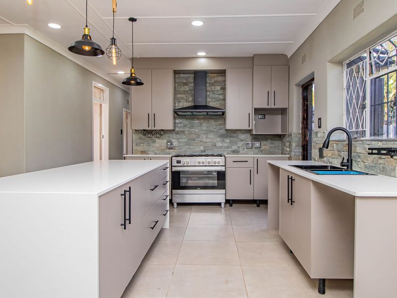 Modern kitchen featuring stone tile backsplash, quartz countertops, gas stove, extractor fan, and ample built-in cabinetry with a central island.