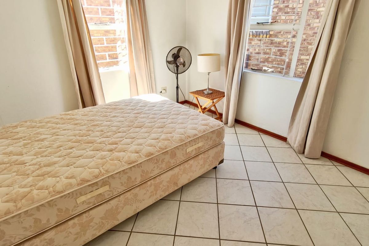 A bedroom featuring tiled flooring and windows with security bars, offering a functional space ready for personal updates and styling.