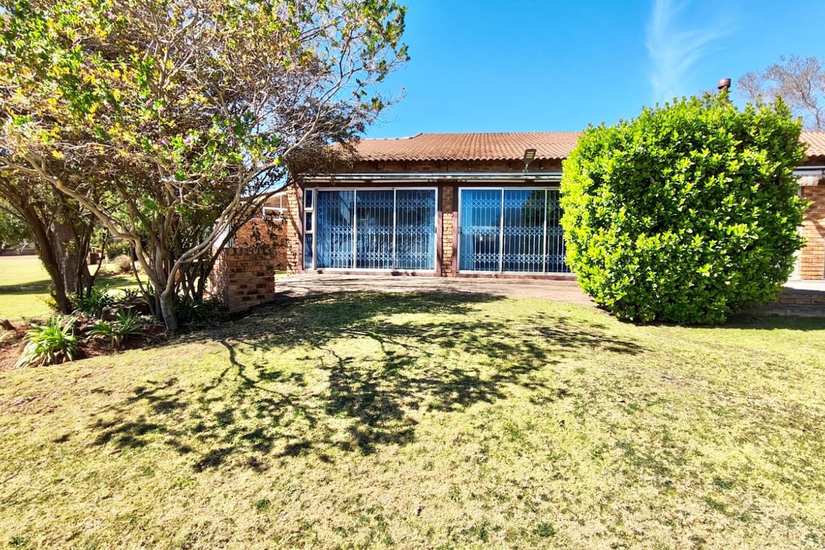 Rear view of the house featuring a brick facade, tiled roof, paved patio area, and large sliding glass doors with security gates.