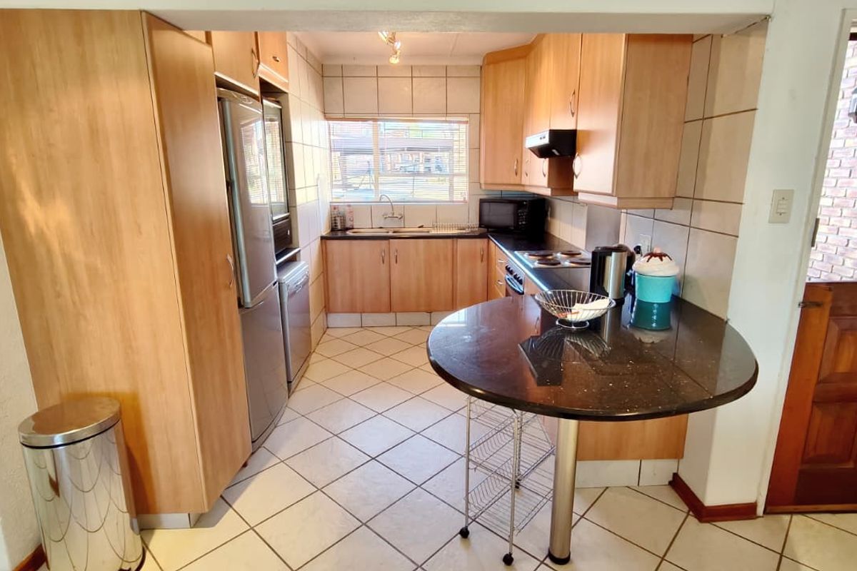 Functional kitchen featuring light wood cabinetry, dark granite-look breakfast bar, tiled backsplash, and ceramic flooring with direct access to an exterior door.