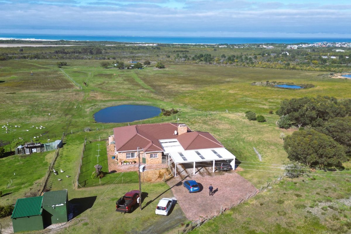 Aerial view of a farm property featuring a main residence with a tiled roof, attached carport, paved driveway, and surrounding rural landscape.