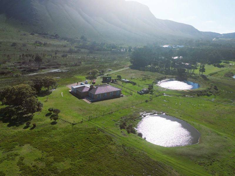 Aerial view of a farmhouse property featuring a tiled roof, surrounding pasture land, and two small dams set against a mountain backdrop.