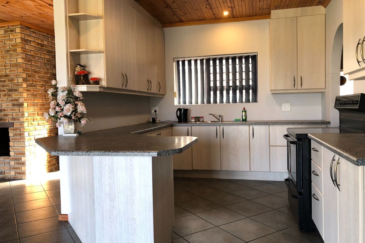 A functional kitchen featuring light wood-look cabinetry, a breakfast bar, tiled flooring, and a distinctive timber-clad ceiling with an adjacent brick feature wall.