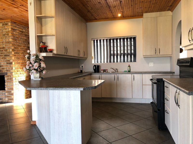 A functional kitchen featuring light wood-look cabinetry, a breakfast bar, tiled flooring, and a distinctive timber-clad ceiling with an adjacent brick feature wall.
