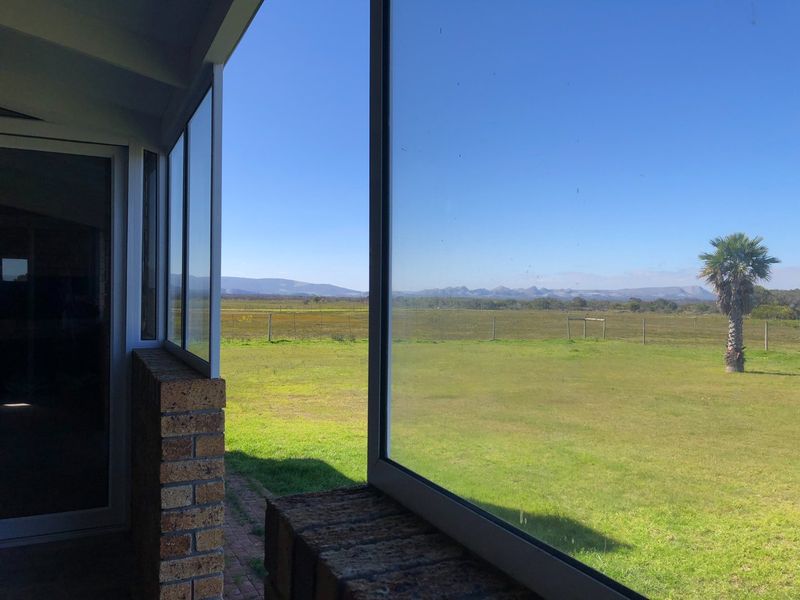 A covered patio area featuring brick masonry and large glass windows, offering expansive views of the surrounding farm landscape.