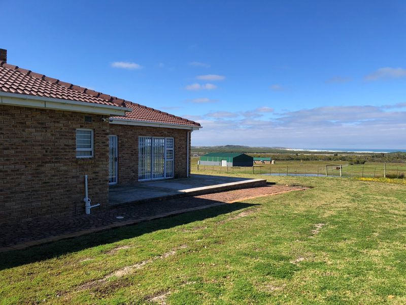 Rear view of the brick farmhouse featuring a concrete patio, security fixtures, and expansive views of the surrounding rural landscape and distant coastline.