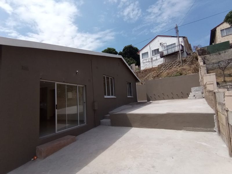 Rear exterior view of the property featuring a concrete patio area, sliding glass door access, and retaining wall structures.
