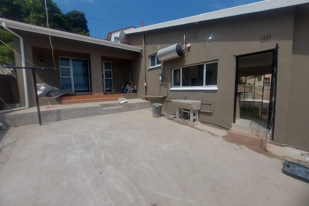 Rear exterior view of the property featuring a concrete patio area, external geyser, and a utility wash trough.
