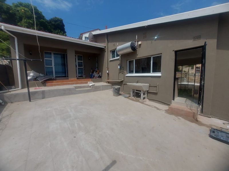 Rear exterior view of the property featuring a concrete patio area, external geyser, and a utility wash trough.