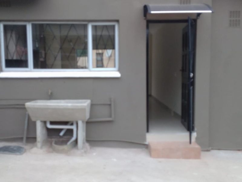 Rear exterior view of the property featuring a concrete laundry trough, solar geyser, and a security-gated entrance.