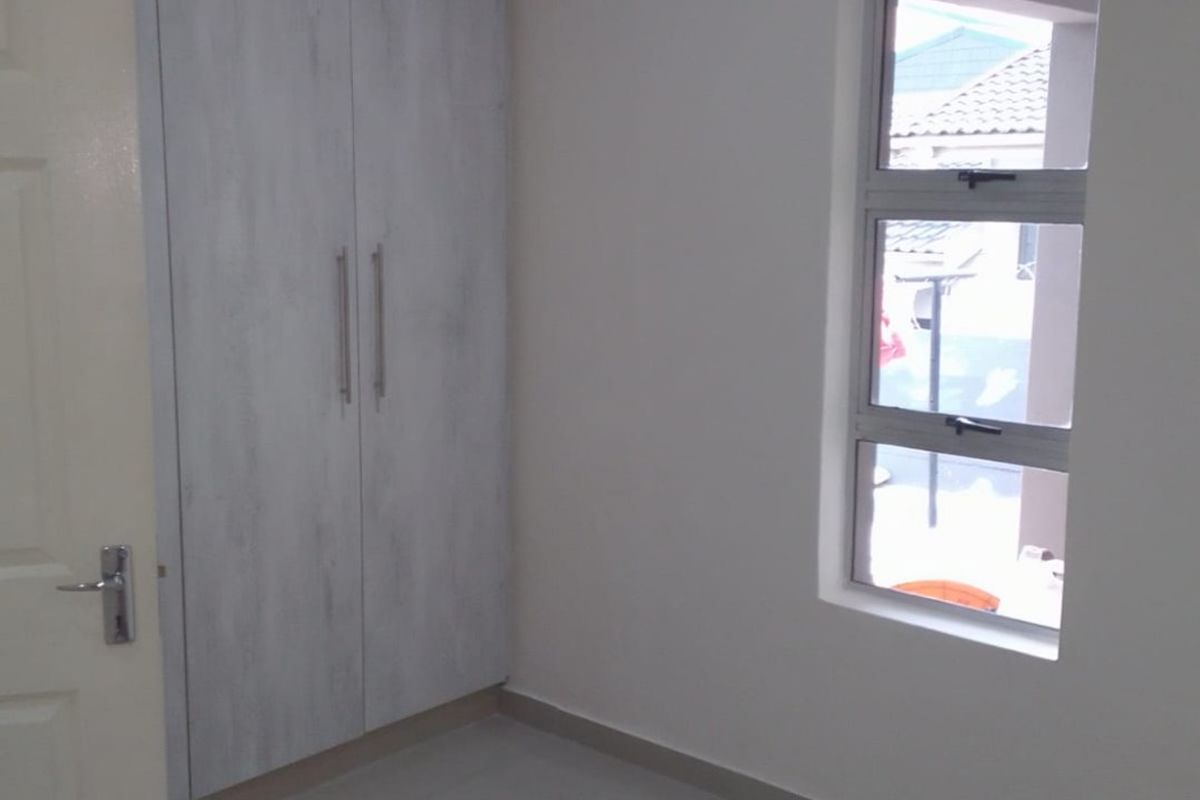A clean, empty bedroom featuring neutral tiled flooring, built-in cupboards, and an aluminium window frame, providing a blank canvas for personalization.