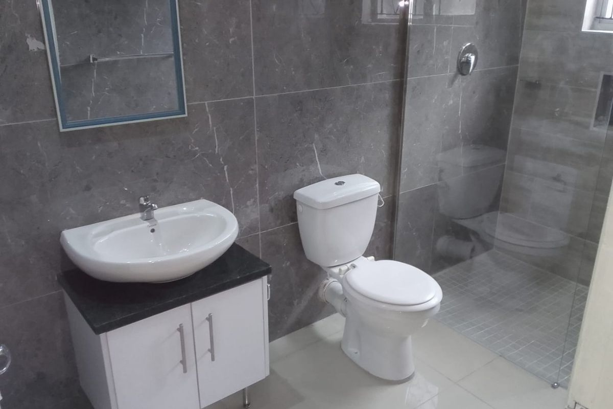 Modern bathroom featuring grey marble-look wall tiles, a white vanity with basin, a toilet, and a glass-enclosed shower area.