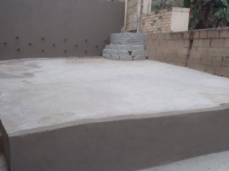 An outdoor concrete patio area featuring a retaining wall and steps, currently in an unfinished state and ready for landscaping or further development.
