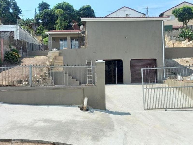Front exterior view of a multi-level house featuring a concrete driveway, metal security gate, garage access, and tiered retaining walls.