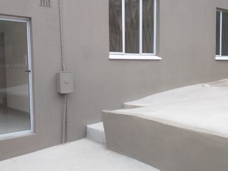 A clean, freshly painted rear exterior view featuring a concrete patio, sliding glass door, and aluminium window frames.