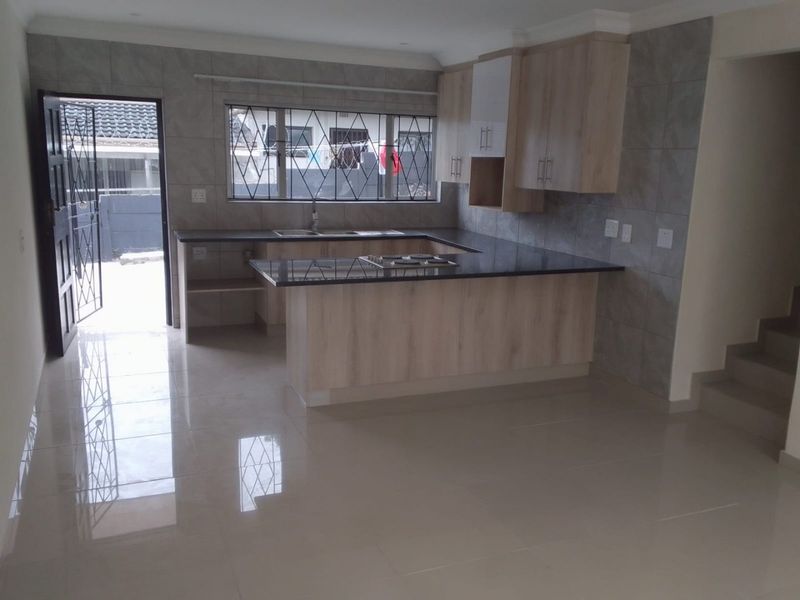 Modern kitchen featuring light wood cabinetry, granite countertops, integrated hob, and tiled finishes, offering a clean and functional workspace.
