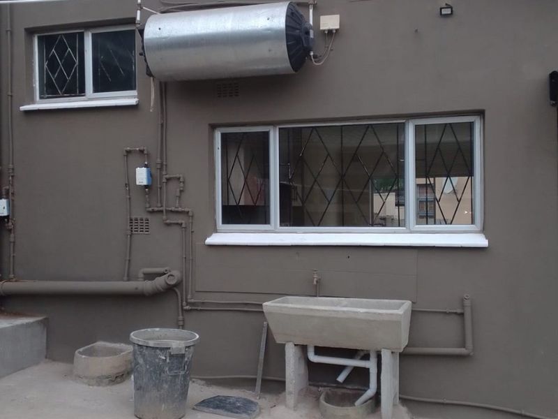 Rear exterior view showing an external geyser, concrete laundry basin, and security-barred windows on a painted masonry wall.