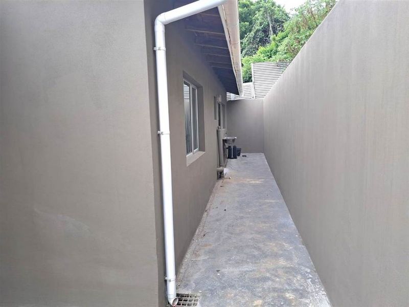 A narrow side passage featuring a concrete pathway, boundary wall, and external sink with a functional downpipe system.