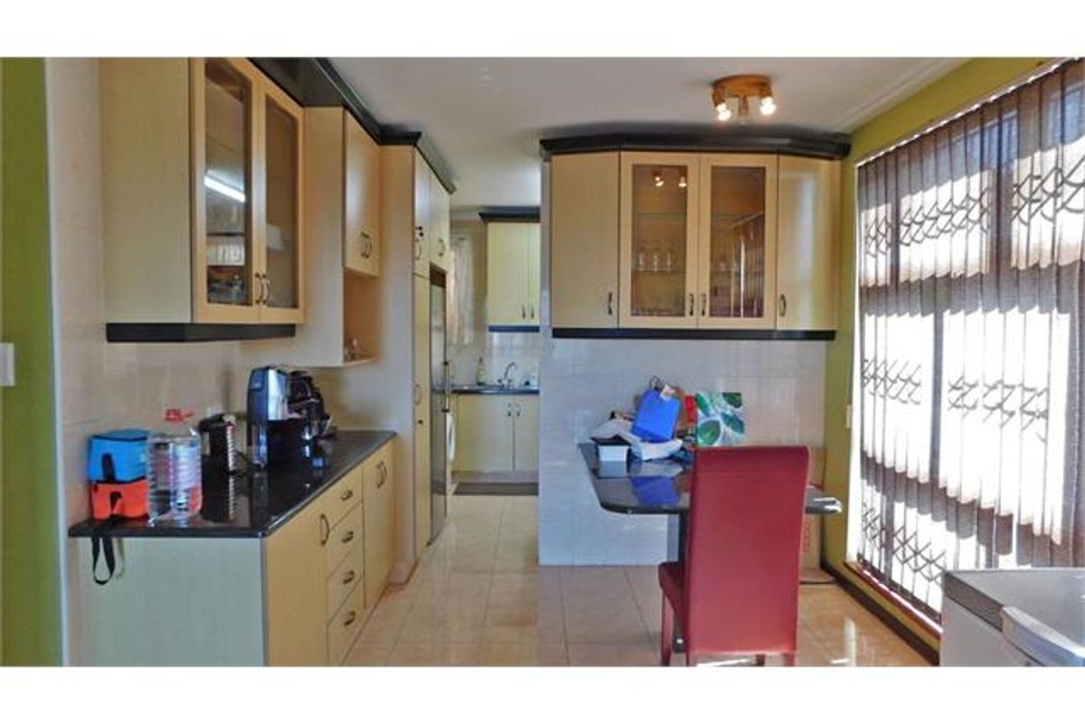 A functional kitchen featuring laminate cabinetry, granite countertops, and tiled flooring, with a secondary prep area visible in the background.