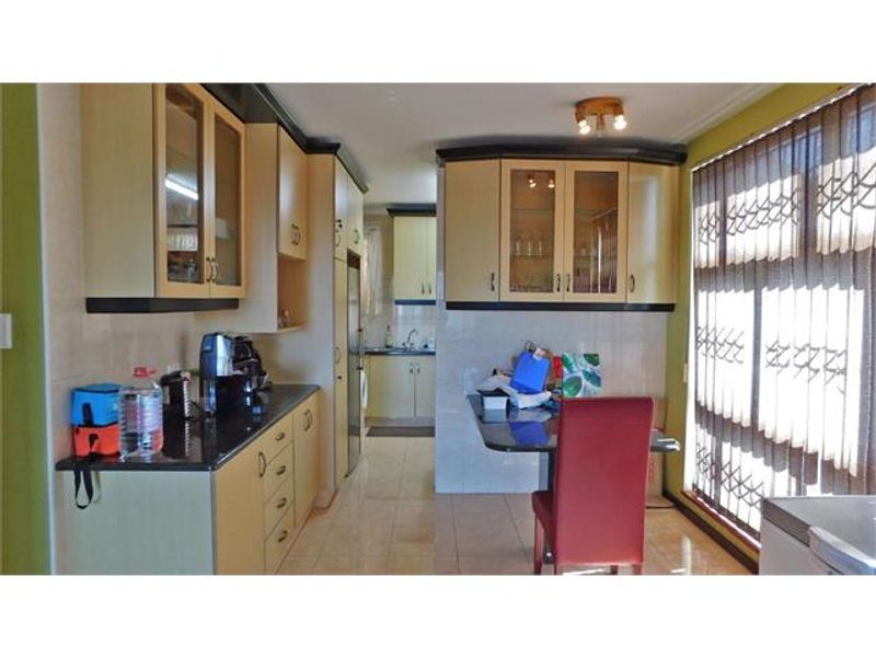 A functional kitchen featuring laminate cabinetry, granite countertops, and tiled flooring, with a secondary prep area visible in the background.