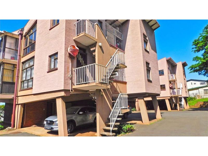 Exterior view of a multi-story apartment building featuring stilt-supported parking, external staircases, and brick facade construction.