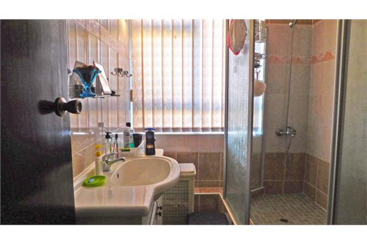 A functional bathroom featuring a vanity basin, a glass-enclosed shower, and tiled walls with vertical blinds for privacy.