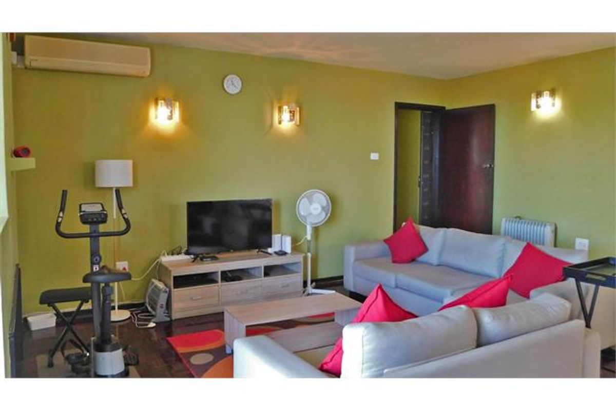 A living room featuring wall-mounted air conditioning, wall sconce lighting, and a radiator, providing a functional space for relaxation.