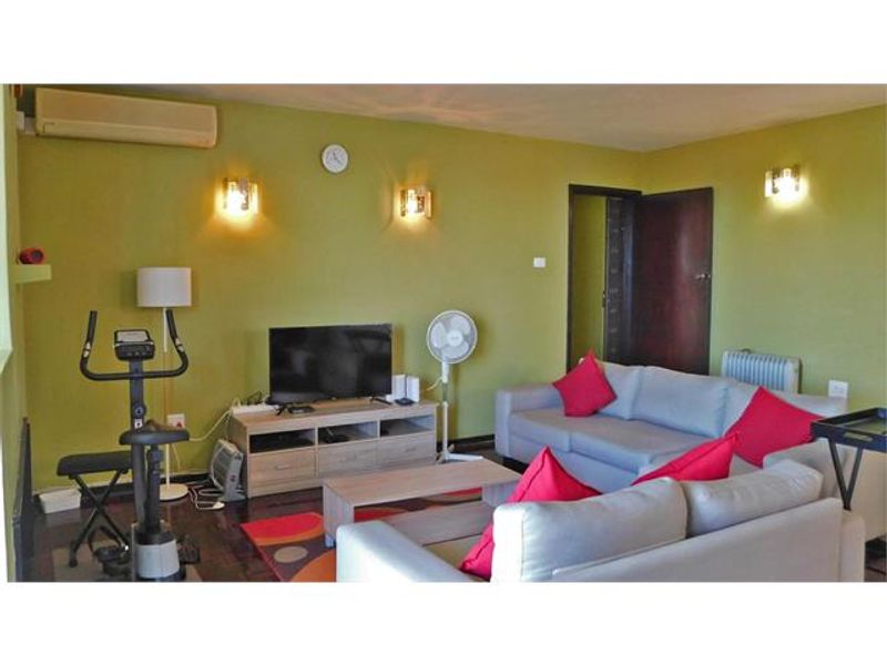 A living room featuring wall-mounted air conditioning, wall sconce lighting, and a radiator, providing a functional space for relaxation.